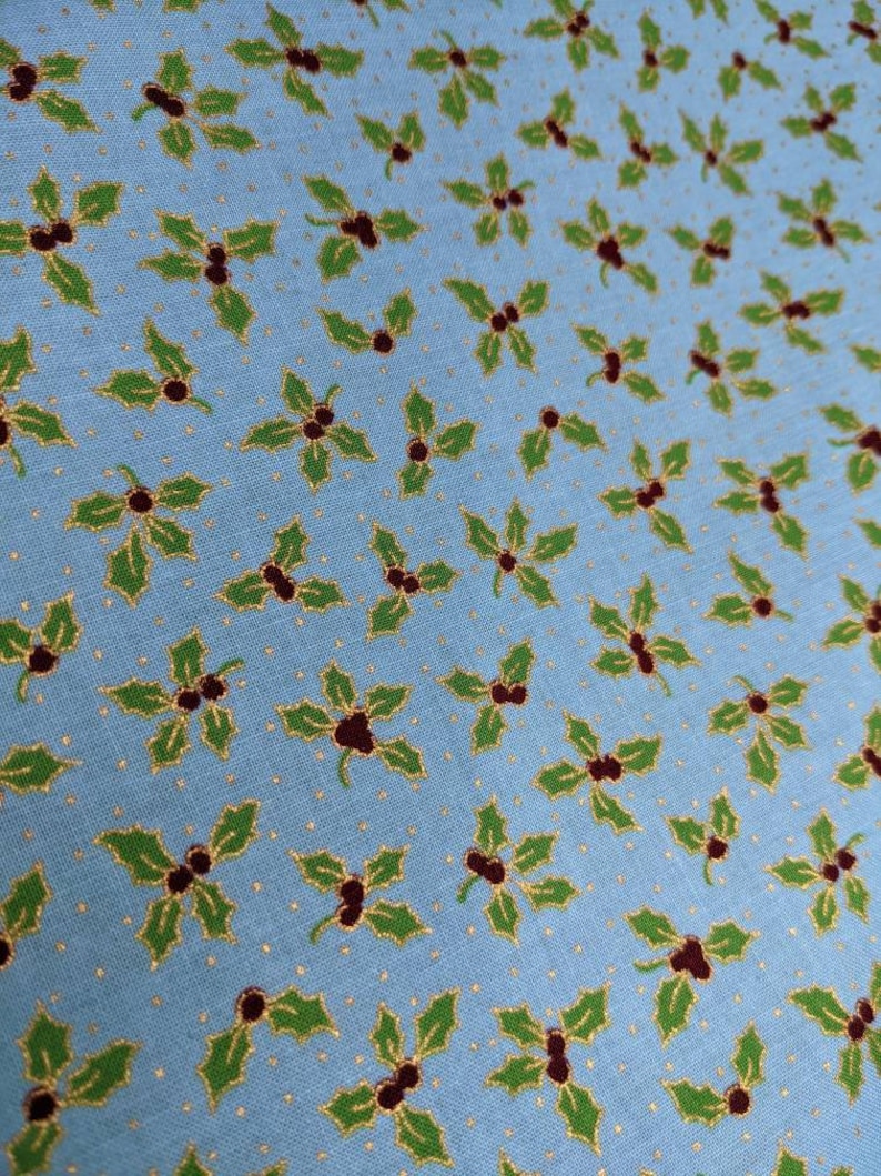 May include: A light blue fabric with a repeating pattern of green holly leaves and red berries. The background is a light blue with a subtle gold glitter pattern.