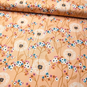 May include: Peach-coloured fabric with a repeating floral pattern. The design features white dandelion-like flowers, small clusters of blue, pink, and orange blossoms, and brown stems. The fabric is folded, showing the pattern's continuity.