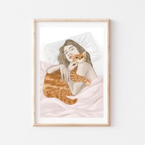 May include: Art print of a person and a ginger cat. The person is lying in bed, holding the cat close. The cat is orange with white markings. The artwork is framed in a light wood frame and set against a white background.