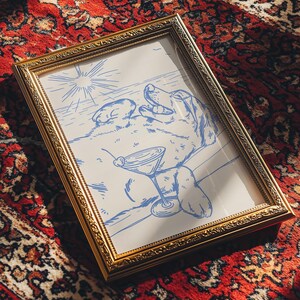 May include: A framed art print featuring a blue line drawing of a dog relaxing with a martini. The artwork is in a gold-colored ornate frame, set against a red patterned rug.