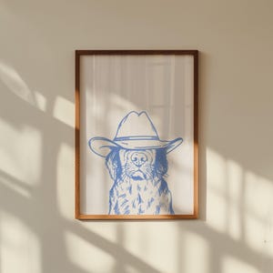 May include: A framed print featuring a blue line drawing of a dog wearing a cowboy hat. The artwork is set against a neutral background, framed in a wooden frame. The dog's face is detailed with visible fur and facial features.