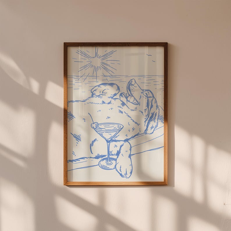 May include: A framed print featuring a blue line drawing of a dog relaxing with a cocktail. The dog is lying on its back, with a martini glass in its paw. The background depicts a beach scene with the sun and ocean.