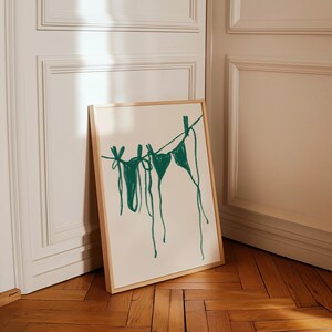 May include: A framed print of a green line drawing of two bikini tops hanging on a clothesline.