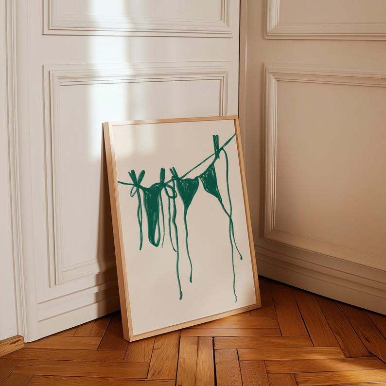 May include: A framed print of a green line drawing of two bikini tops hanging on a clothesline.