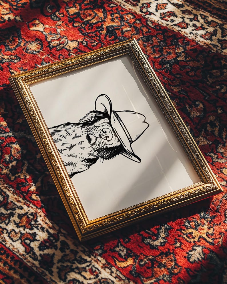 Puede incluir: Un dibujo en blanco y negro de un perro con un sombrero de vaquero. El dibujo est&aacute; enmarcado en un marco dorado y est&aacute; sobre una alfombra de patr&oacute;n rojo y blanco.