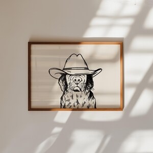 Puede incluir: Una ilustraci&oacute;n en blanco y negro de un perro con un sombrero de vaquero. El perro est&aacute; mirando directamente al espectador. La ilustraci&oacute;n est&aacute; enmarcada en un marco de madera marr&oacute;n claro.