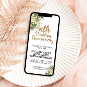 May include: A smartphone displays a golden 50th Wedding Anniversary invitation. The text includes the date, time, and location of the event. Floral accents and a white background enhance the design. The phone rests on a white plate with a soft pink background.