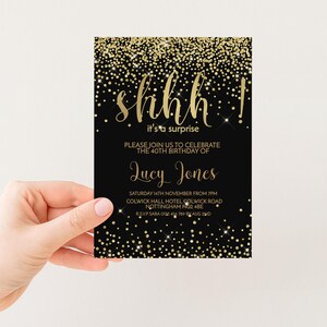a hand holding a black and gold birthday invitation card with a glittery design.