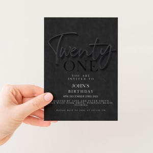A person is holding a black invitation card with text and details about a birthday party.