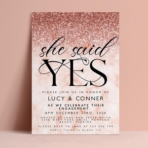 The image is a wedding invitation featuring a pink and gold glittery background with the text "she said yes" prominently displayed.
