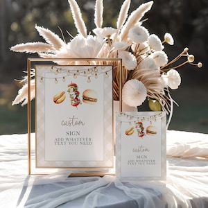 May include: Two custom signs with gold frames and a watercolor illustration of a hot dog, kebab, and burger. The signs have the text "custom SIGN ADD WHATEVER TEXT YOU NEED" and are decorated with string lights. A floral arrangement is in the background.
