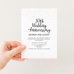 a hand holding a white wedding anniversary invitation card with a black and white design.