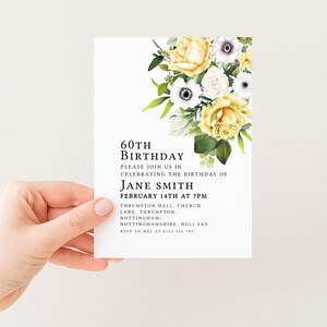 A hand holding a white invitation card with a floral design and text inviting guests to a birthday celebration.