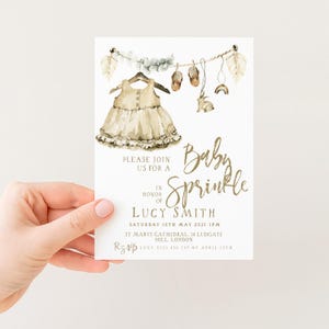 The image is a hand holding a baby shower invitation card.