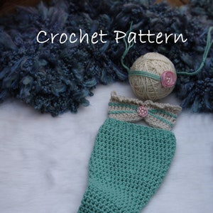 May include: A crocheted mermaid tail costume for a baby, in teal green with a cream and brown crocheted top and a pink flower embellishment.  The costume is laid out on a white surface.  "Crochet Pattern" is written in white text at the top of the image.