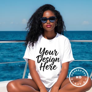 Könnte beinhalten: Ein weißes T-Shirt mit dem Text "Your Design Here" in schwarzer Schrift. Das Model trägt eine Sonnenbrille und goldene Creolen. Der Hintergrund ist ein blauer Ozean.