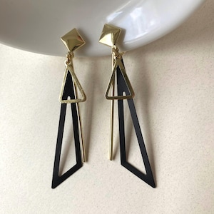May include: Geometric dangle earrings with a gold square stud, a gold triangle, and a black geometric shape. The earrings have a modern, minimalist design.