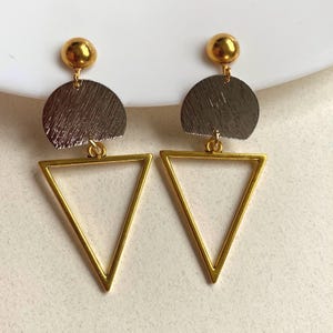 May include: A pair of gold-colored geometric earrings. Each earring features a gold ball stud, a silver-colored half-circle, and a gold triangle. The earrings are designed with a modern, minimalist aesthetic.