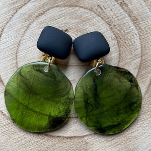 May include: A pair of green and black clip-on earrings. The earrings feature a round green resin piece with black marbling and a black square piece on top.