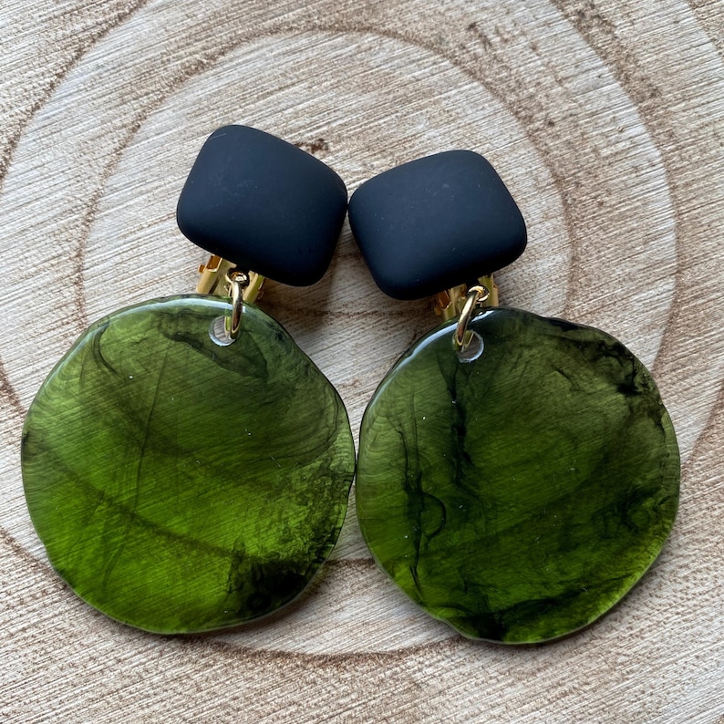 May include: A pair of green and black clip-on earrings. The earrings feature a round green resin piece with black marbling and a black square piece on top.