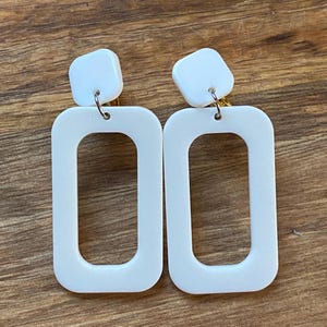 May include: A pair of white rectangular clip-on earrings with a smaller square shape at the top.
