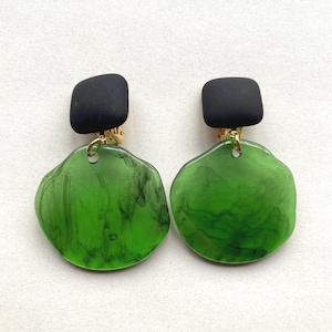 A pair of green dangling circle clip on earrings hanging from square black clips.