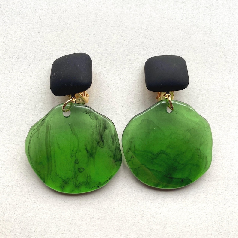 A pair of green dangling circle clip on earrings hanging from square black clips.