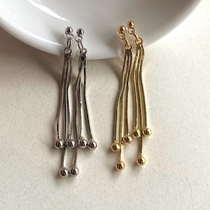 May include: A pair of dangle earrings, one silver-toned and one gold-toned. Each earring features a small ball at the top, with multiple strands of chain ending in small, round beads. The earrings are displayed on a white surface.