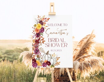 May include: A white welcome sign with a floral wreath in shades of burgundy, orange, and yellow. The sign reads "Welcome to Samantha's Bridal Shower 10.23.2023".