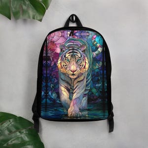May include: A black backpack featuring a vibrant, multi-coloured graphic print of a tiger on the front panel. The tiger design incorporates a stained-glass aesthetic with shades of blue, purple, pink, and yellow, set against a dark background.