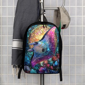 May include: A black backpack featuring a vibrant, stained-glass style graphic of a manta ray swimming amidst colorful aquatic flora. The design incorporates shades of blue, purple, pink, and gold, set against a circular, glowing background pattern.