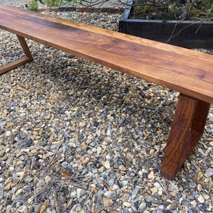 May include: A wooden bench with a dark brown finish and a simple, modern design. The bench has a rectangular top and two angled legs.