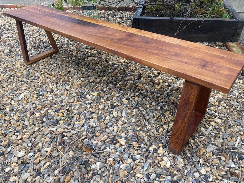May include: A wooden bench with a dark brown finish and a simple, modern design. The bench has a rectangular top and two angled legs.