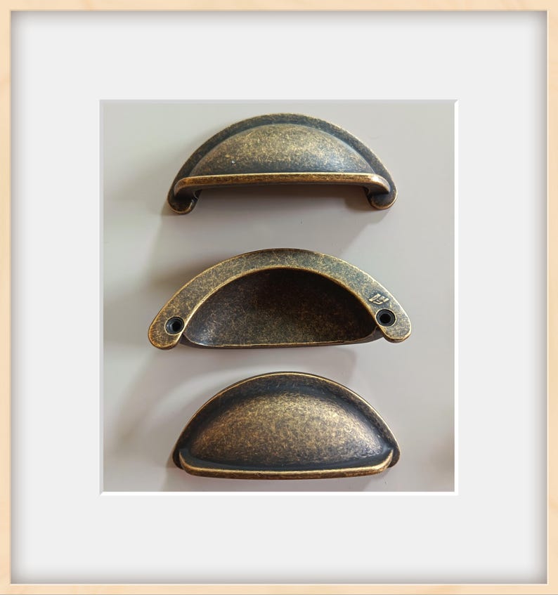May include: Three antique-style cabinet pulls with a bronze finish. Each pull has a half-moon shape with a textured surface and two screw holes. The pulls are arranged vertically against a neutral background, showcasing their design.