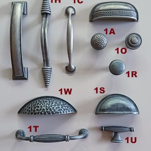 May include: A selection of pewter-effect cabinet handles and knobs. Designs include a curved handle, a textured knob, and a half-moon pull. The hardware is displayed against a neutral background. The text "The Pewter collection" is at the bottom.