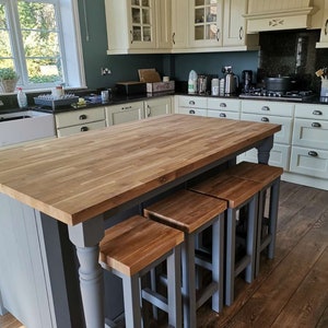 May include: A kitchen featuring cream-colored cabinets, a dark countertop, and a large wooden island. The island has a grey base and a wooden countertop, with four wooden stools. The walls are painted a dark teal colour.