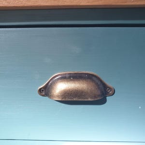 May include: A close-up of a drawer with a brass pull handle. The drawer is painted a light teal blue colour.