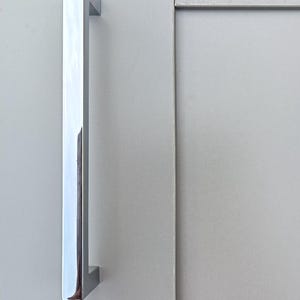 May include: A silver, rectangular door handle with a smooth, polished finish.