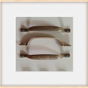 May include: Three antique bronze cabinet pulls. Two are straight with rounded ends, and one is a curved handle. Each pull has a distressed finish and is mounted with small screws, offering a vintage aesthetic for furniture restoration or new builds.
