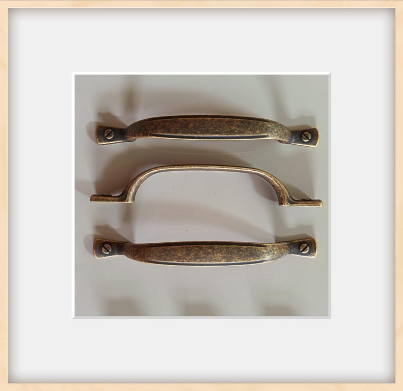 May include: Three antique bronze cabinet pulls. Two are straight with rounded ends, and one is a curved handle. Each pull has a distressed finish and is mounted with small screws, offering a vintage aesthetic for furniture restoration or new builds.