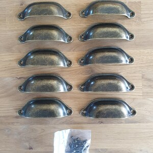May include: Ten antique brass cabinet pulls with a rounded, arched shape. The pulls are arranged in two rows of five. A small bag of screws is included.