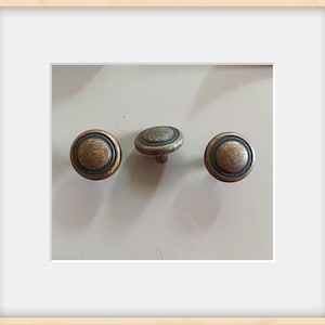 May include: Three antique bronze cabinet knobs with a circular design. Each knob features a raised center and a dark ring around the edge. The knobs are set against a light background.