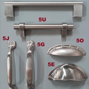 May include: A collection of brushed nickel cabinet hardware, including pulls, knobs, and handles. The hardware is displayed on a light blue background. The text "The Brushed Steel Collection" is printed below the hardware.