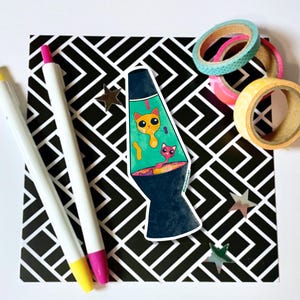 May include: A sticker of a blue lava lamp with two orange and pink cats inside. The sticker is on a black and white patterned background.