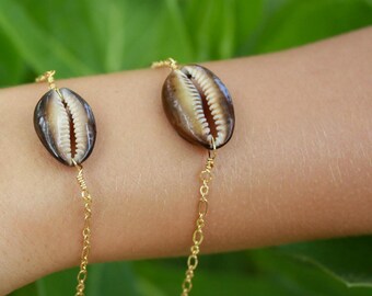 May include: A gold chain bracelet with two brown cowrie shells. The shells are attached to the chain with gold wire.