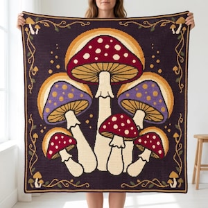 May include: A square crochet blanket featuring a dark purple background with a central design of five mushrooms in red, white, and purple with yellow accents. The border is decorated with thin, winding vines and small mushroom motifs in yellow and green.