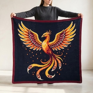 May include: A square crochet blanket featuring a dark navy blue background with a central phoenix design in vibrant shades of orange, yellow, and deep red. The phoenix has large, outstretched wings and a long, flowing tail, framed by a dark red border.