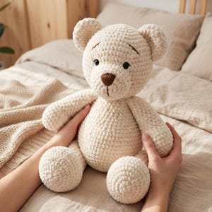 May include: A cream-colored crochet teddy bear featuring a soft, textured yarn finish, small black bead eyes, and a dark brown embroidered nose. The stuffed animal has rounded ears, a round belly, and articulated limbs in a seated position.