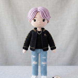 May include: A handmade crochet doll with purple hair, wearing a black jacket with gold accents, a black shirt, ripped blue jeans, and white sneakers. A silver chain necklace and a black and white light stick are also included.
