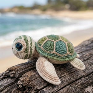 May include: A crocheted sea turtle with large, expressive eyes. The turtle features a green and beige shell, a striped head, and beige flippers. It is resting on a piece of driftwood, with a blurred beach and ocean background.
